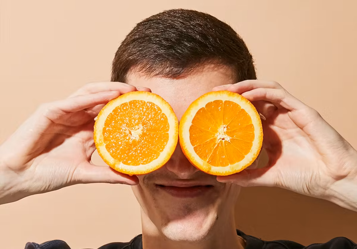 Lächelnde Person hält zwei Orangenhälften vor das Gesicht